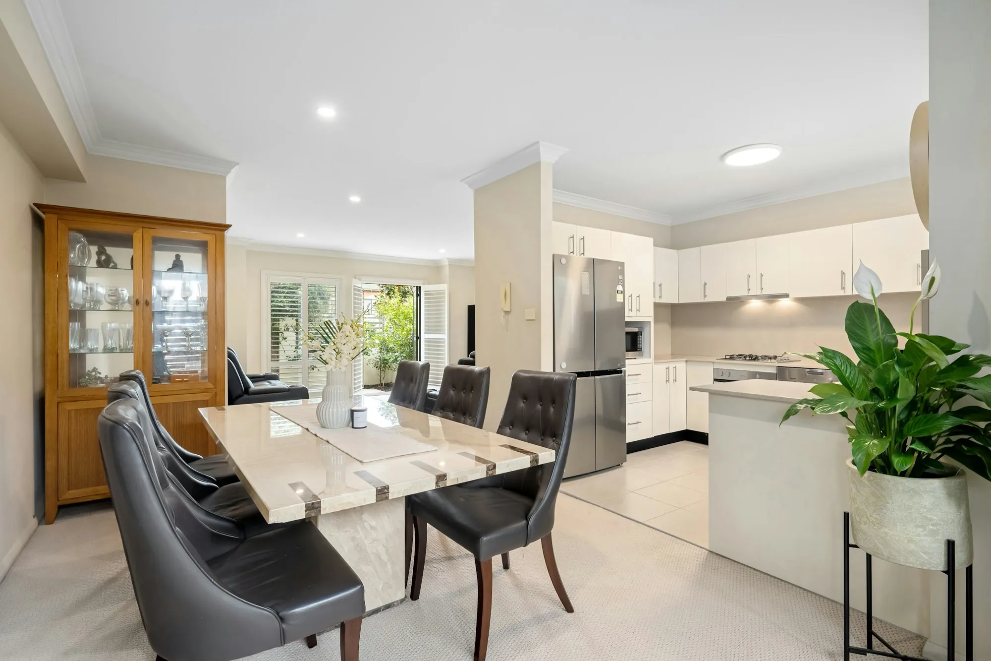 Glass dining table near an open kitchen and tall plants