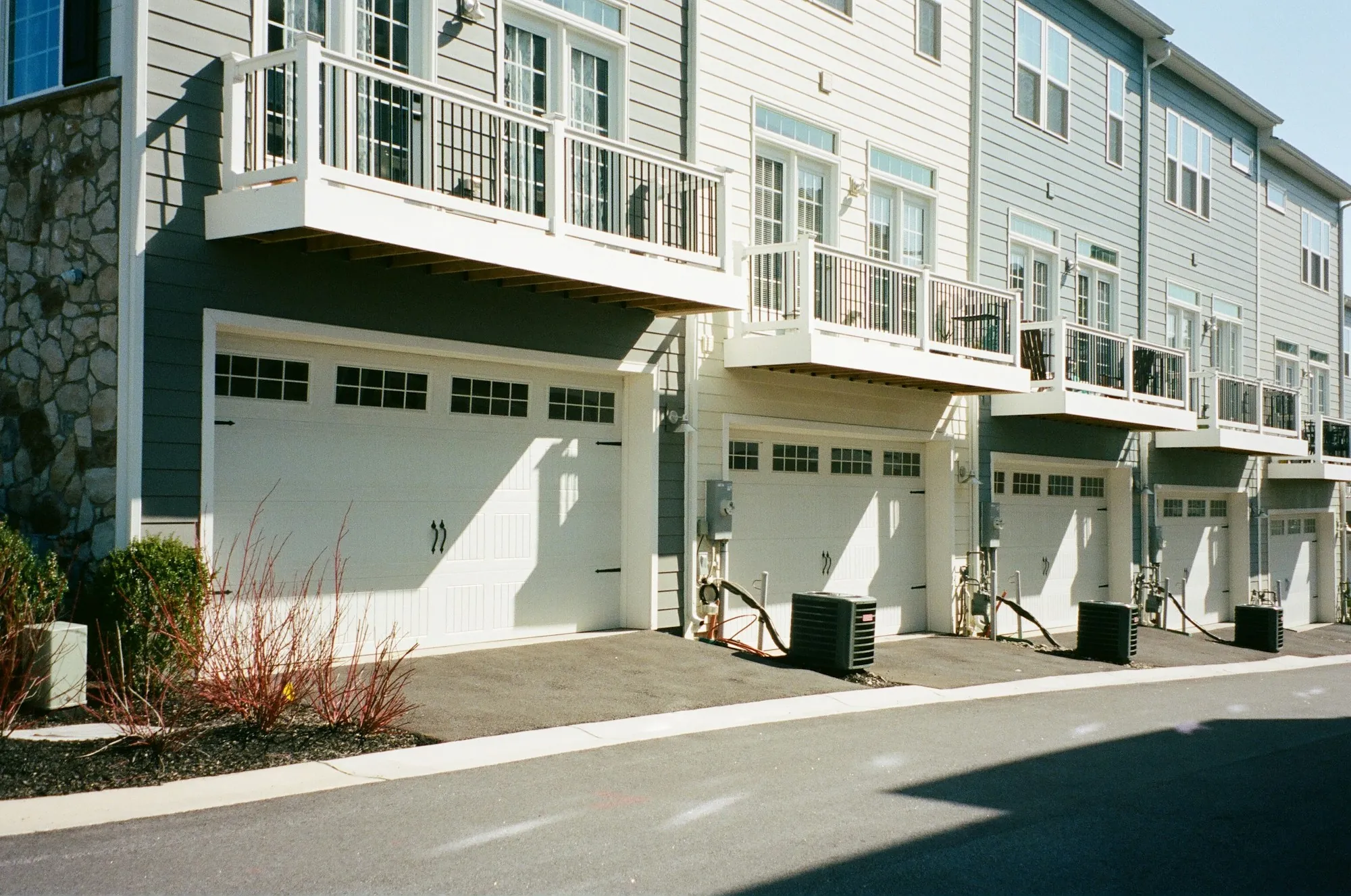 Townhouses with garages and balconies along a sunny street